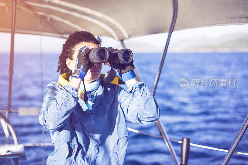 Young woman sailing, looking with binoculars